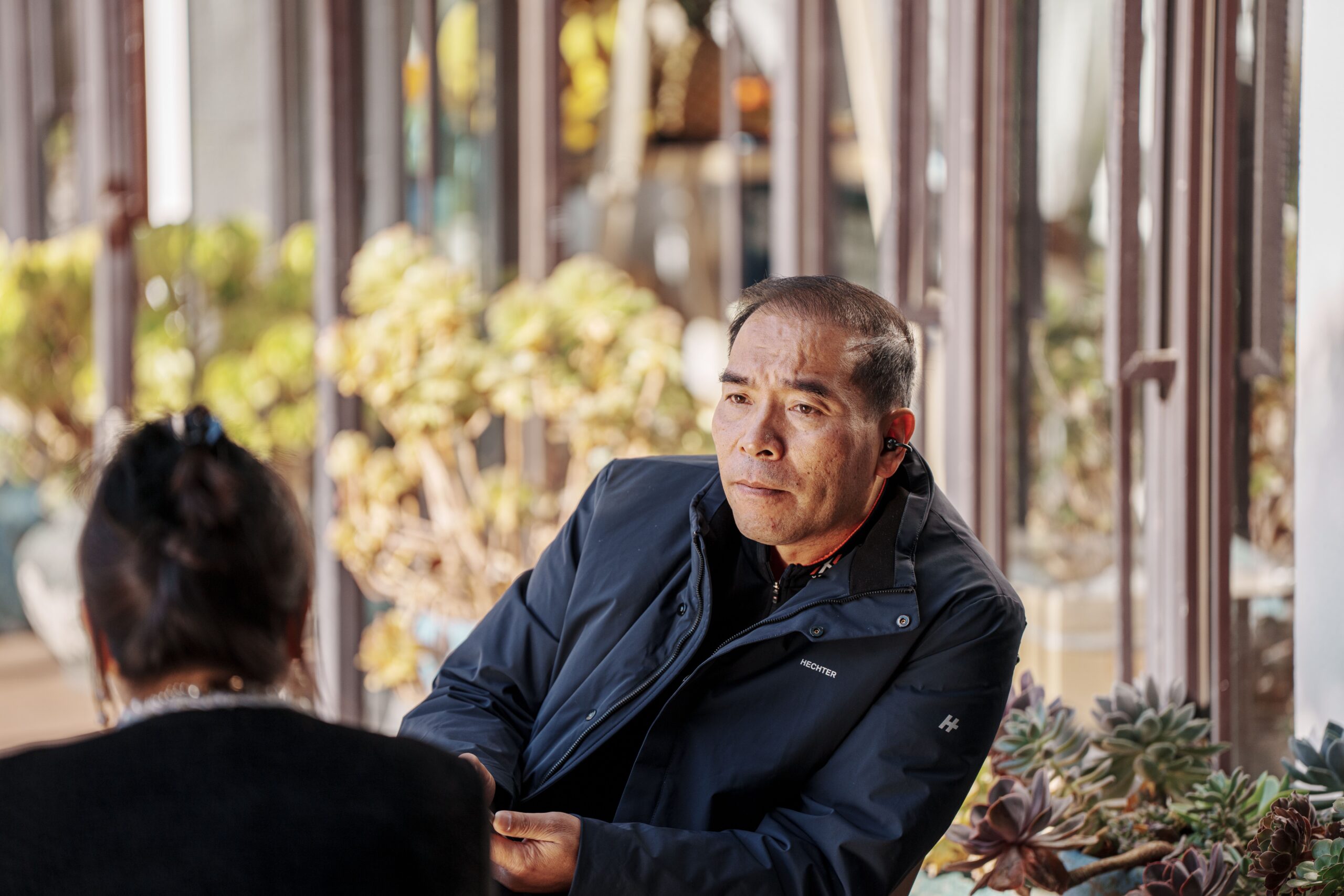 Two adults engaged in a relaxed, genuine conversation at a sunny outdoor cafe