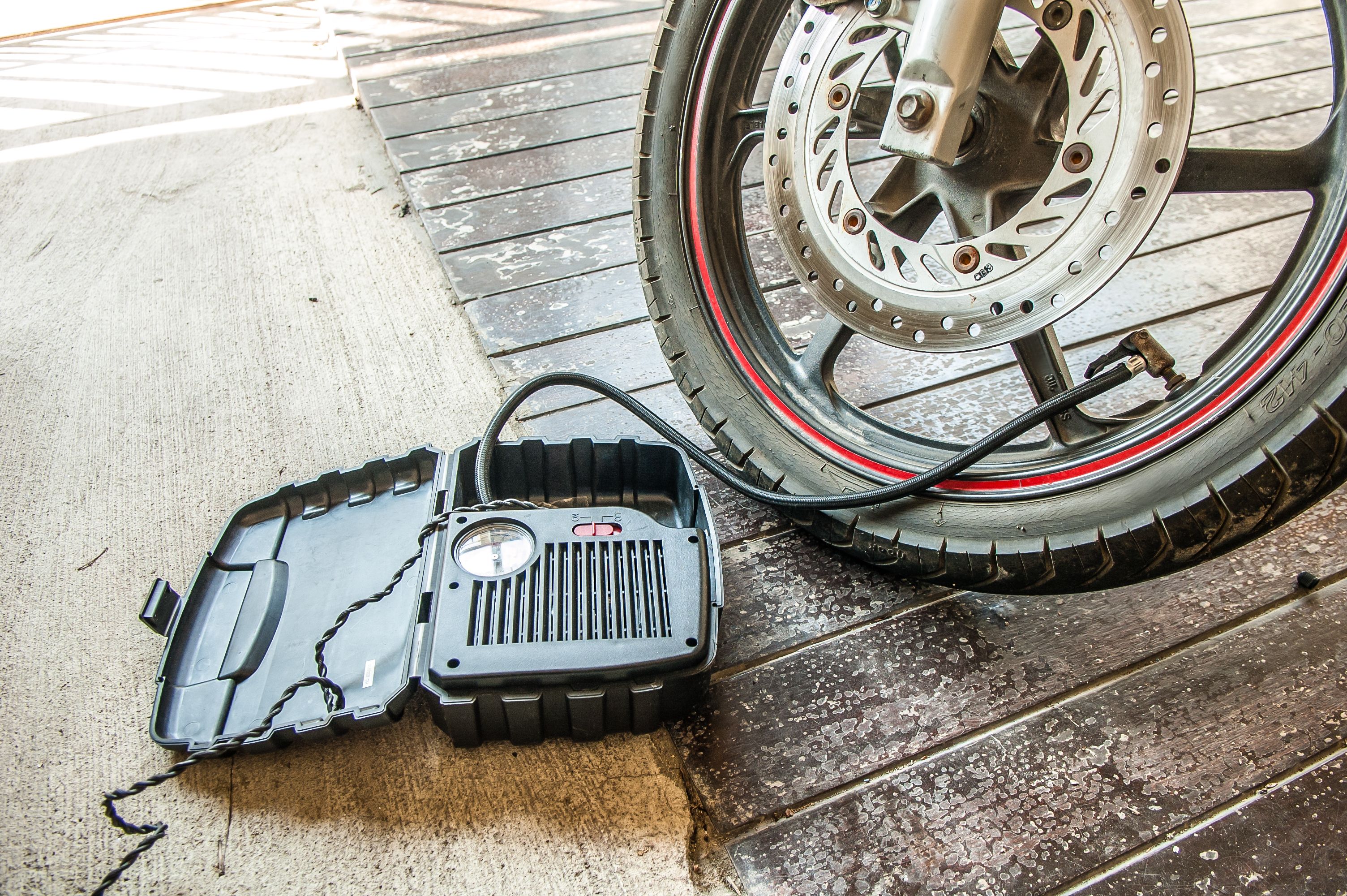Close-up of a motorcycle tire being inflated with a portable air pump before a trip.