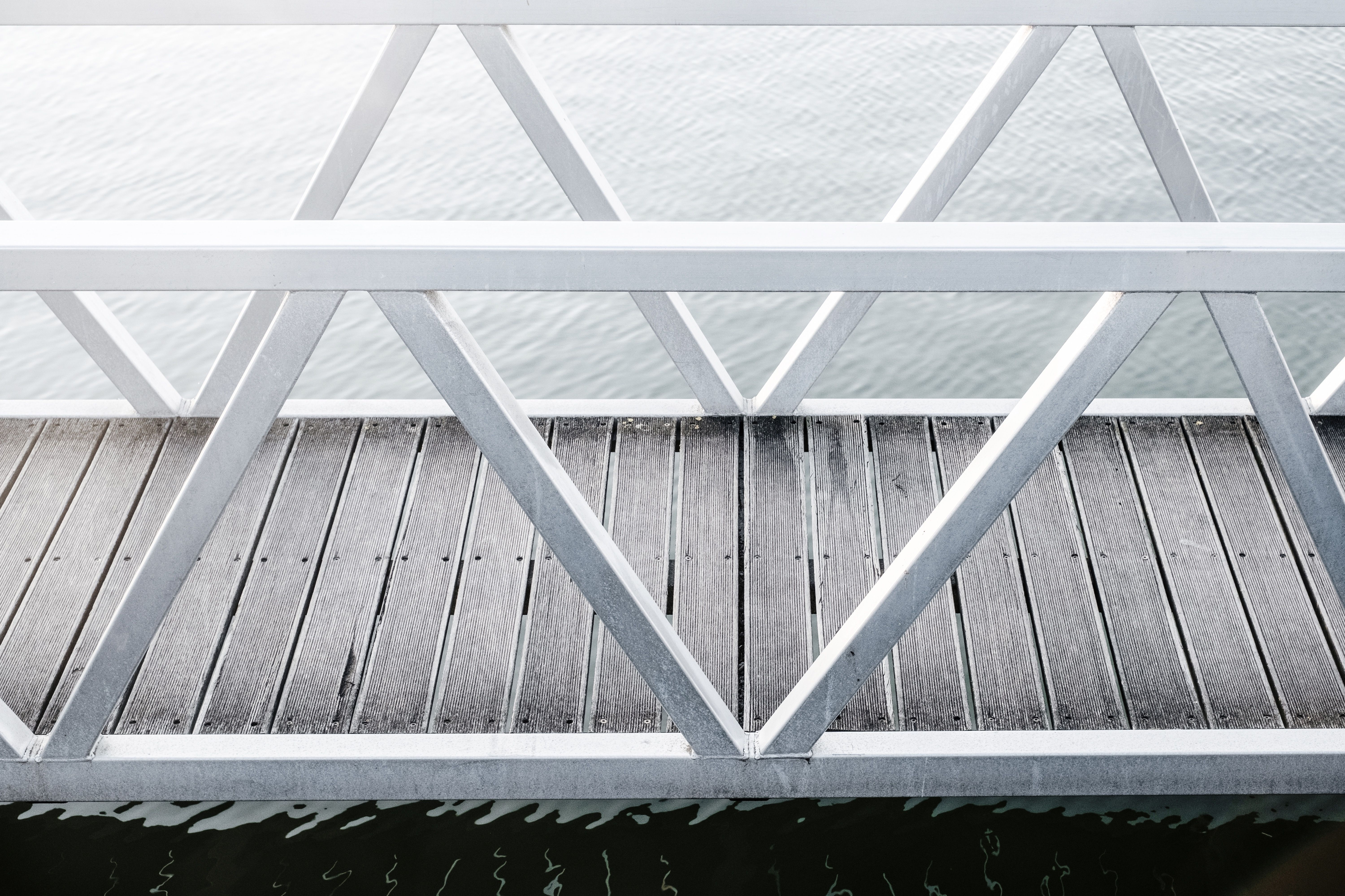 Minimalist dock with metal railings beside calm water, evoking durable outdoor metal construction in a weather-exposed setting.